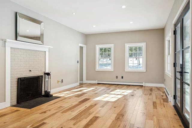 unfurnished living room with a baseboard heating unit, a brick fireplace, and light wood-type flooring