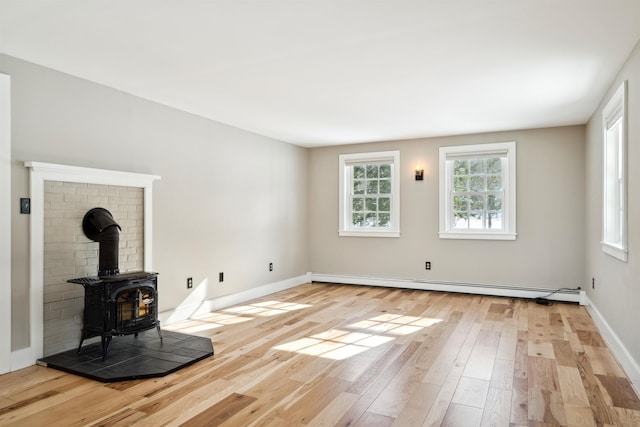 unfurnished living room with light wood-type flooring, a wood stove, and baseboard heating