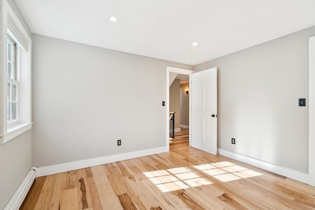 spare room featuring a baseboard heating unit and light wood-type flooring