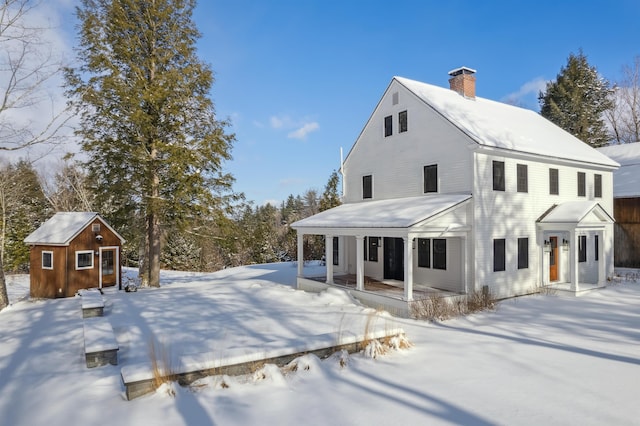 snow covered rear of property with a porch and a shed