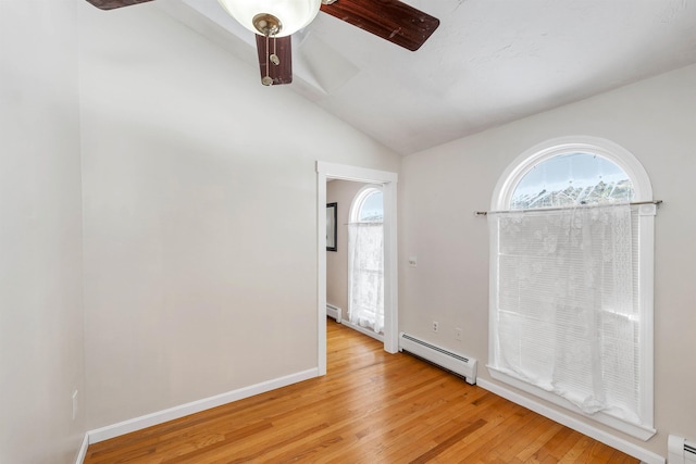 spare room featuring baseboard heating, lofted ceiling, and light wood-type flooring