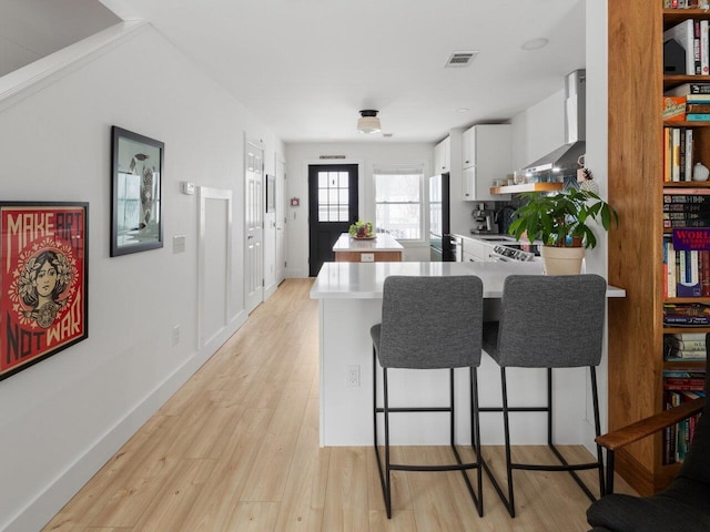 kitchen featuring white cabinets, fridge, wall chimney exhaust hood, kitchen peninsula, and light hardwood / wood-style flooring