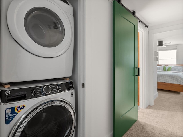 laundry area with stacked washer / drying machine, a barn door, and carpet flooring