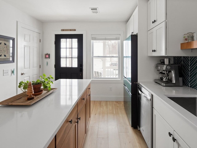 kitchen featuring black fridge, light wood-type flooring, stainless steel dishwasher, white cabinets, and backsplash