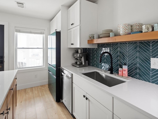 kitchen with sink, light hardwood / wood-style flooring, black refrigerator, white cabinetry, and stainless steel dishwasher