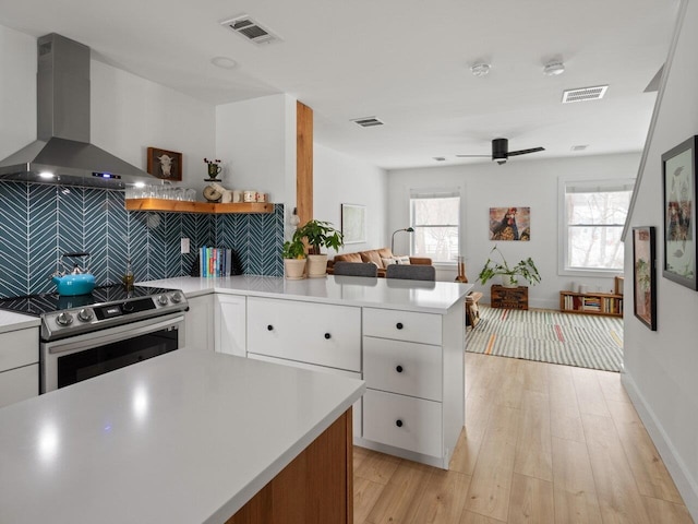 kitchen featuring wall chimney exhaust hood, white cabinetry, tasteful backsplash, stainless steel electric range, and light wood-type flooring