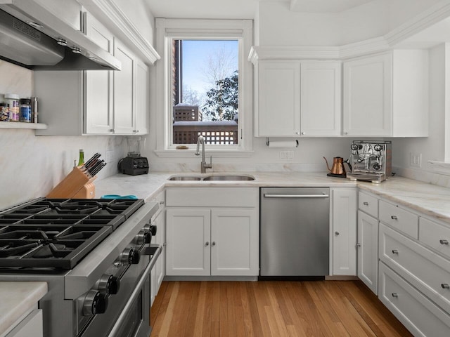 kitchen featuring appliances with stainless steel finishes, wall chimney exhaust hood, sink, and white cabinets