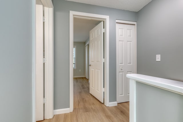 corridor with a textured ceiling and light wood-type flooring