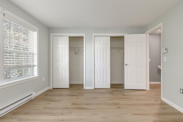 unfurnished bedroom featuring light wood-type flooring, multiple closets, and baseboard heating