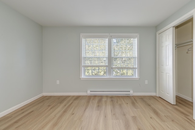 unfurnished bedroom featuring baseboard heating, a closet, and light hardwood / wood-style flooring