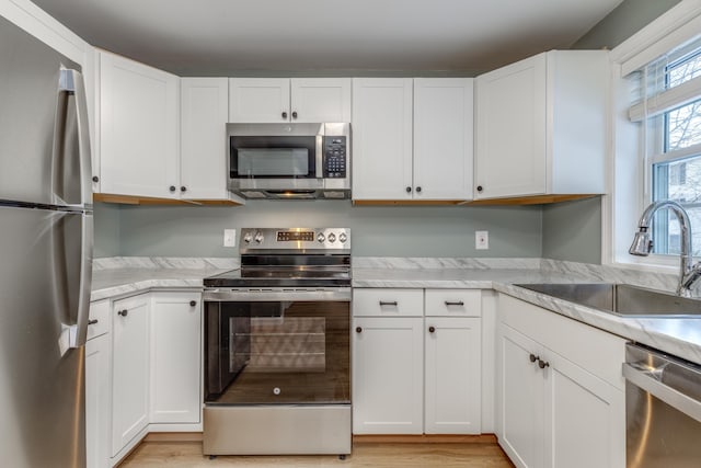 kitchen with appliances with stainless steel finishes, light hardwood / wood-style floors, sink, and white cabinets