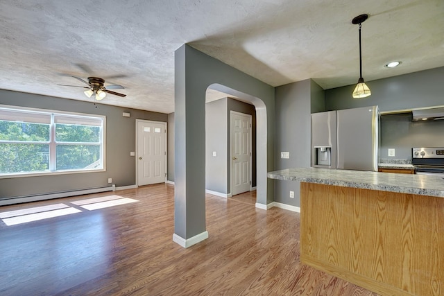 kitchen with appliances with stainless steel finishes, a baseboard heating unit, extractor fan, decorative light fixtures, and light wood-type flooring