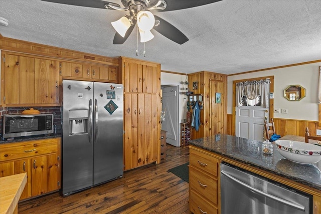 kitchen featuring a textured ceiling, ornamental molding, wooden walls, appliances with stainless steel finishes, and dark hardwood / wood-style flooring