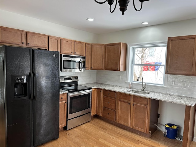 kitchen with sink, light stone counters, tasteful backsplash, stainless steel appliances, and light hardwood / wood-style floors