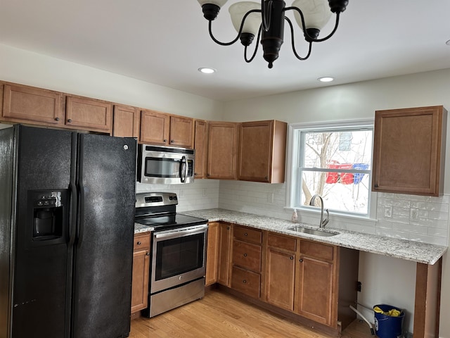 kitchen featuring appliances with stainless steel finishes, sink, backsplash, light stone counters, and light hardwood / wood-style flooring