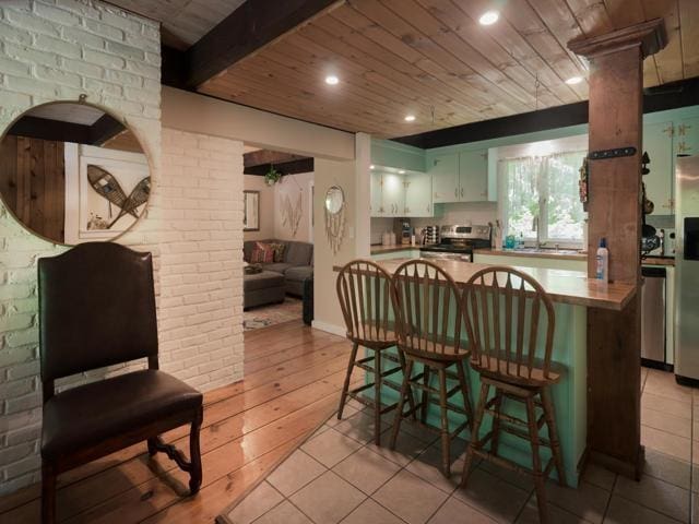 kitchen featuring green cabinetry, wooden ceiling, kitchen peninsula, stainless steel appliances, and beam ceiling