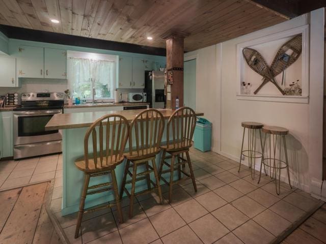 kitchen featuring sink, appliances with stainless steel finishes, wooden ceiling, a kitchen bar, and light tile patterned flooring