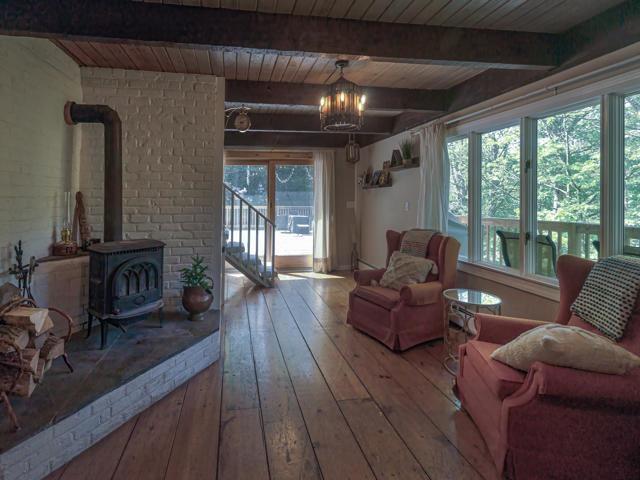 sitting room featuring beamed ceiling, a wood stove, hardwood / wood-style flooring, a notable chandelier, and wood ceiling