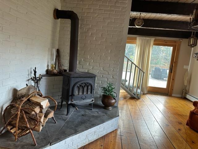 sitting room featuring beamed ceiling, wood-type flooring, brick wall, and a wood stove