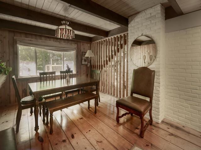 dining room with beamed ceiling, light wood-type flooring, and wood walls