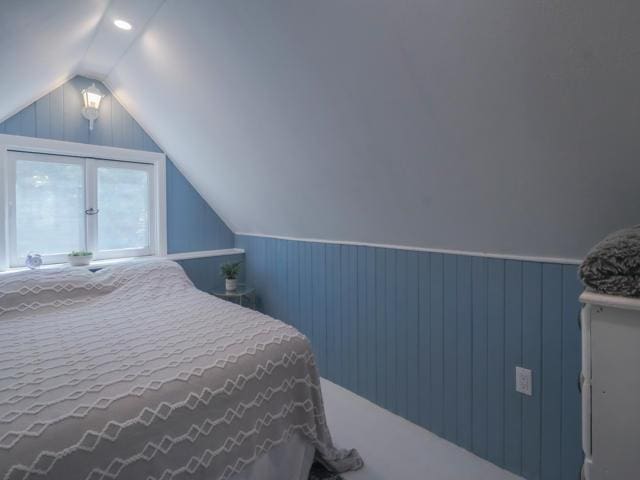 bedroom with vaulted ceiling and wood walls