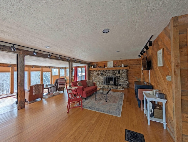 living room featuring light hardwood / wood-style flooring, rail lighting, wooden walls, a fireplace, and a textured ceiling