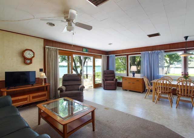 living room with wooden walls, ceiling fan, and a water view