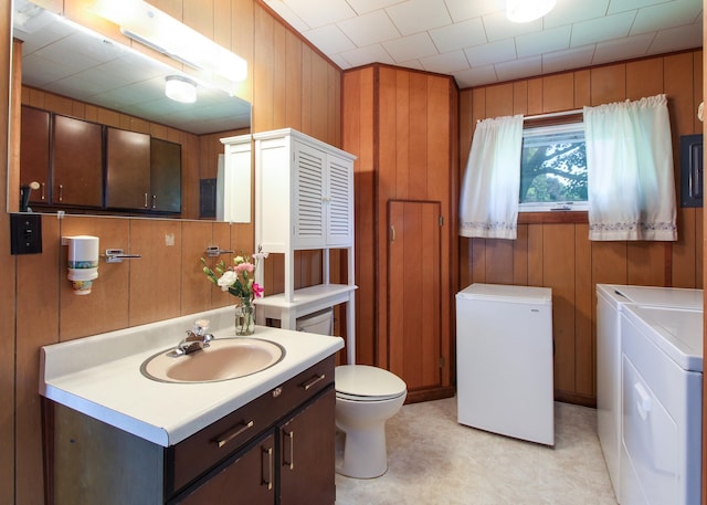 bathroom with vanity, independent washer and dryer, toilet, and wood walls