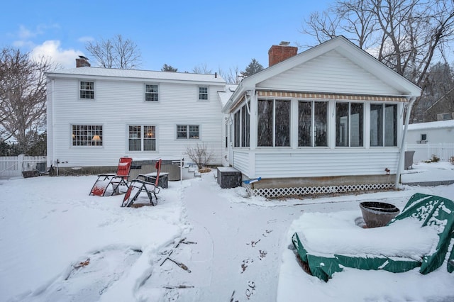 snow covered rear of property with a sunroom