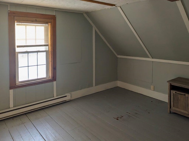 additional living space with wood-type flooring, lofted ceiling, a baseboard heating unit, and a healthy amount of sunlight