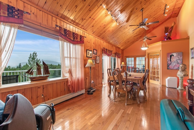 dining area with light wood-type flooring, a wealth of natural light, wooden ceiling, and wood walls