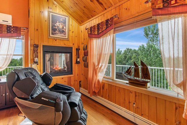 sitting room with vaulted ceiling, a baseboard heating unit, a multi sided fireplace, and wood walls