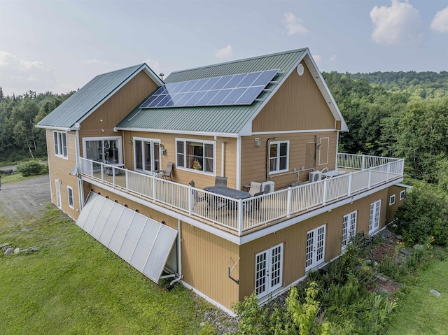 rear view of property featuring french doors, a yard, and solar panels