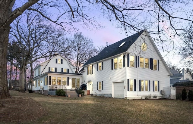 back house at dusk with a garage, covered porch, and a lawn