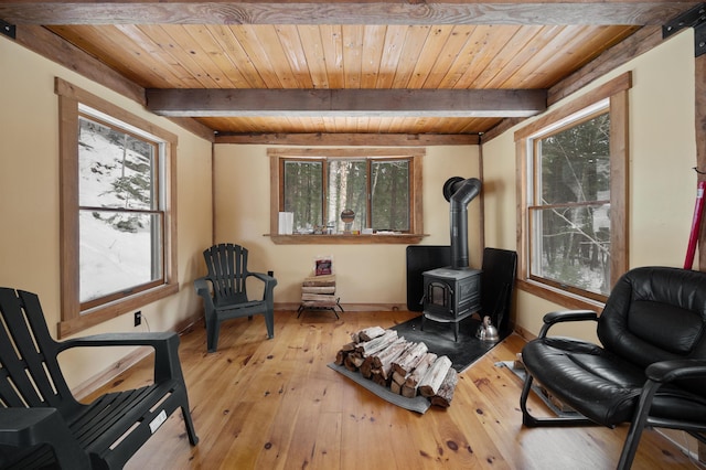 living area featuring beam ceiling, a wood stove, wood ceiling, and light wood-type flooring