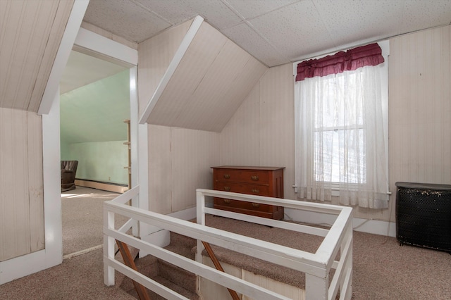 carpeted bedroom featuring vaulted ceiling, wood walls, and baseboard heating