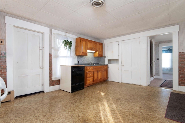 kitchen with a paneled ceiling, brick wall, black dishwasher, and sink