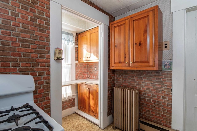 kitchen featuring brick wall, white gas range, radiator, and a paneled ceiling