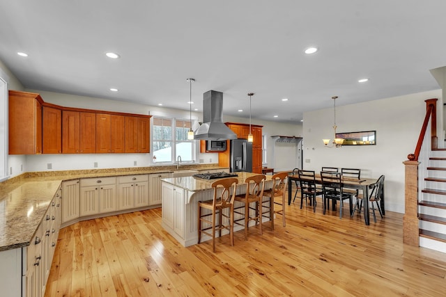 kitchen with a center island, a kitchen breakfast bar, island exhaust hood, stainless steel appliances, and light hardwood / wood-style floors