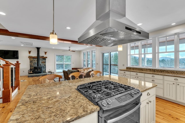 kitchen featuring gas range, a wood stove, island range hood, and light stone counters