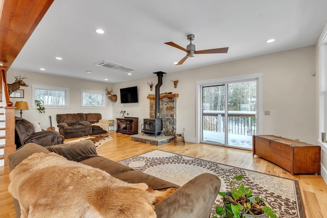 living room featuring ceiling fan, hardwood / wood-style floors, and a wood stove