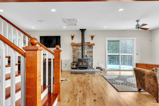 living room featuring light wood-type flooring, ceiling fan, and a wood stove