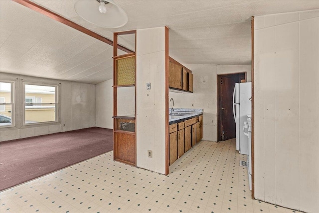 kitchen featuring white refrigerator, lofted ceiling, and sink