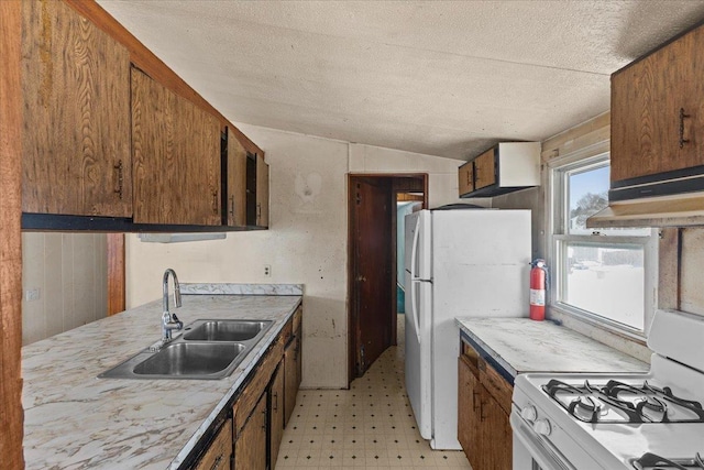 kitchen featuring vaulted ceiling, white appliances, sink, and a textured ceiling