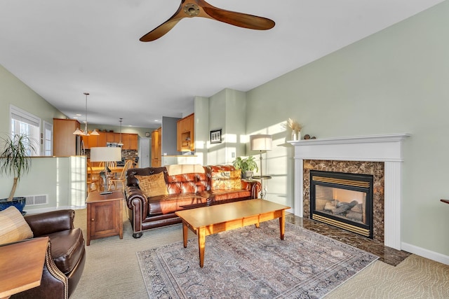 carpeted living room with a high end fireplace and ceiling fan