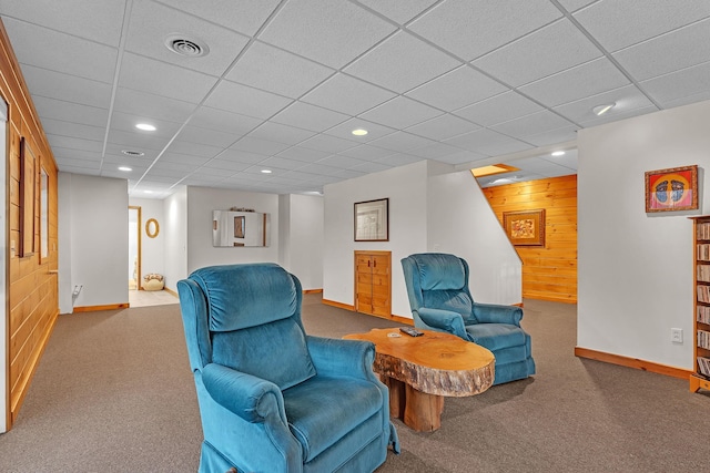 living area with carpet, a drop ceiling, and wooden walls