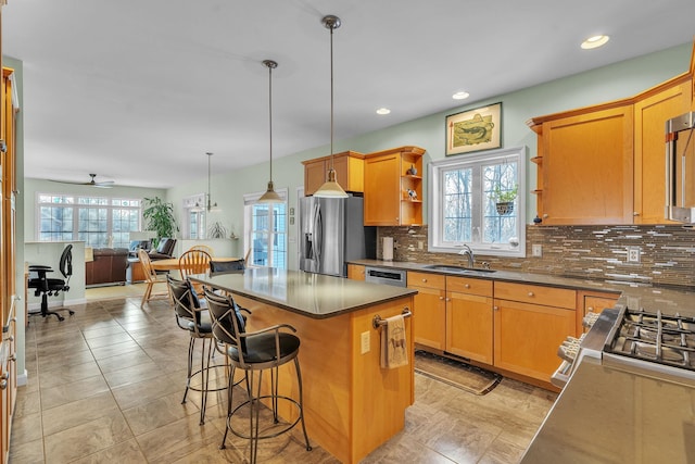 kitchen with sink, appliances with stainless steel finishes, hanging light fixtures, a center island, and a kitchen bar