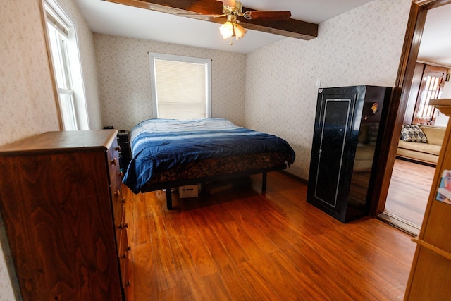 bedroom with hardwood / wood-style flooring, ceiling fan, multiple windows, and beamed ceiling