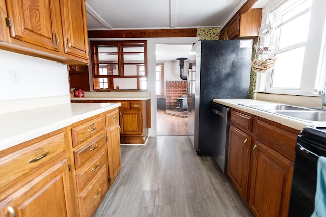 kitchen with sink, crown molding, light wood-type flooring, a wood stove, and appliances with stainless steel finishes