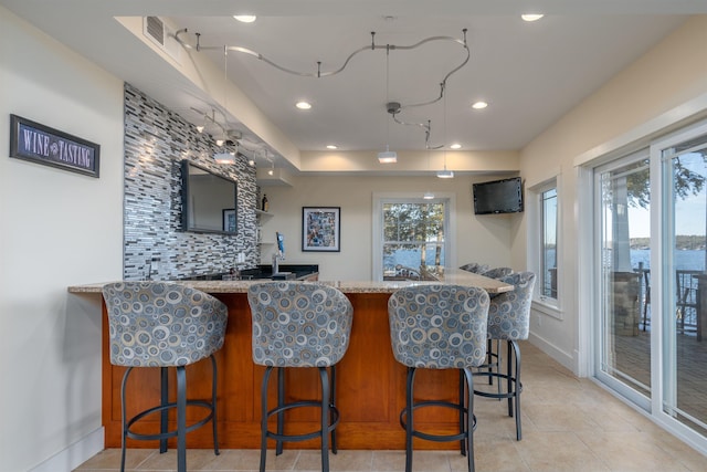 bar with light tile patterned floors, decorative backsplash, and light stone countertops